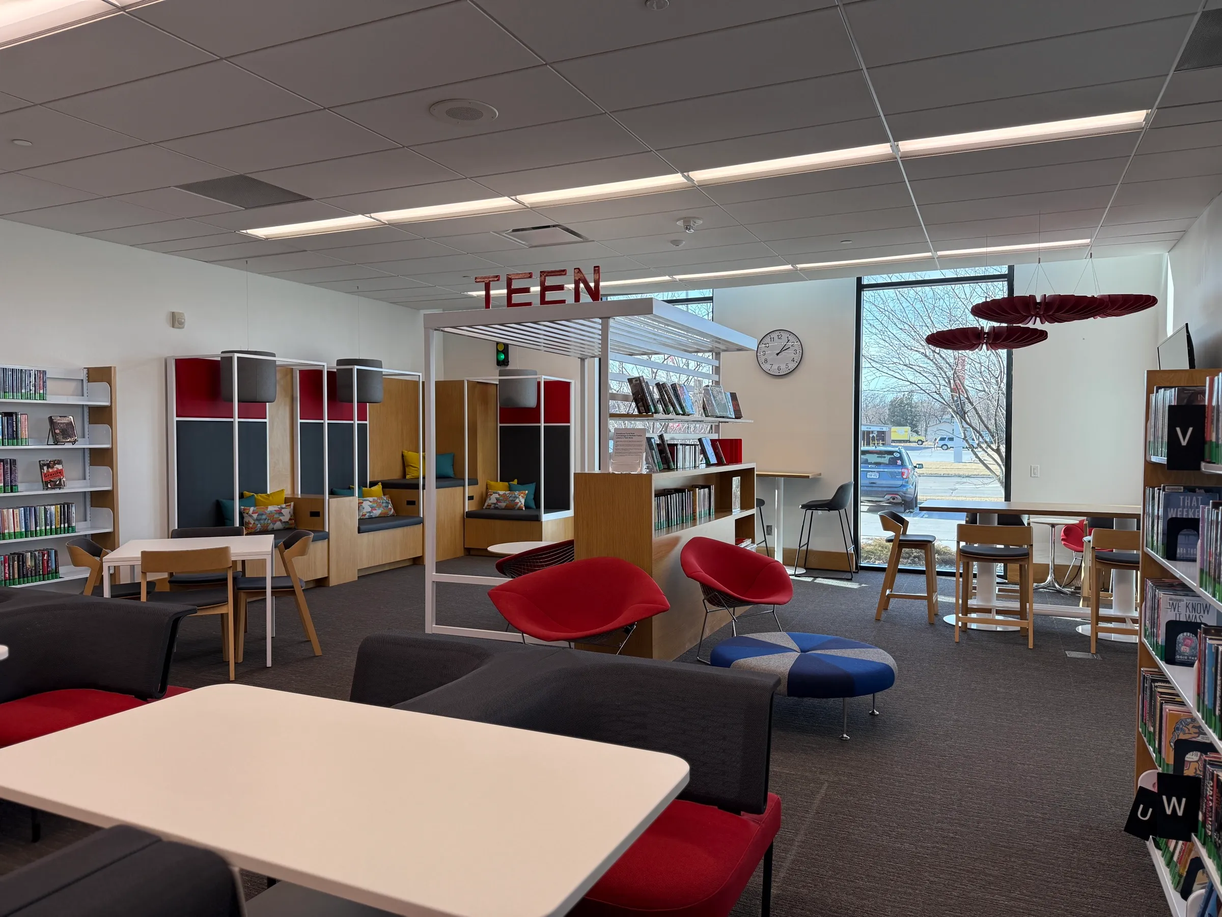 Library teen area with red wire chairs, study tables and low shelving